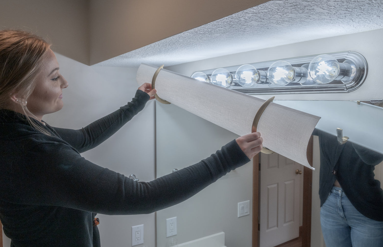 A woman is covering a silver beveled edge Hollywood light with a a 36" shade