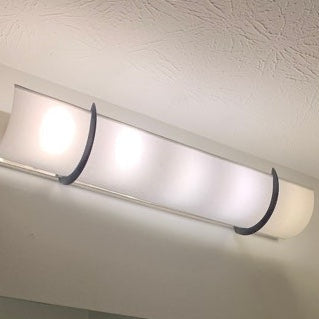 Hollywood light covered by a shantung white EzLightWrap shade with black brackets, hides a vanity light