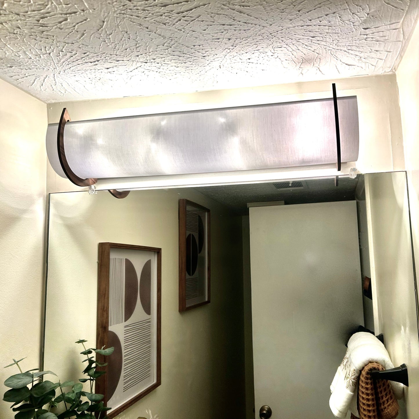 A 25" modern rectangular EzLightWrap frosted white shantung shade and walnut accents, mounted above a bathroom mirror reflecting a hallway and framed art.