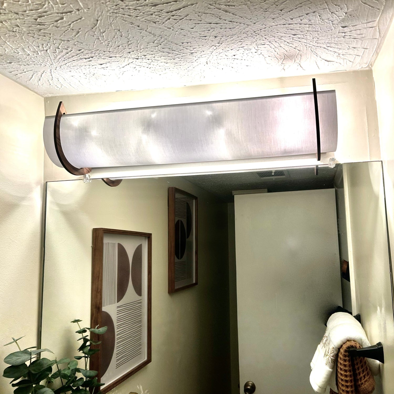 A 25" modern rectangular EzLightWrap frosted white shantung shade and walnut accents, mounted above a bathroom mirror reflecting a hallway and framed art.