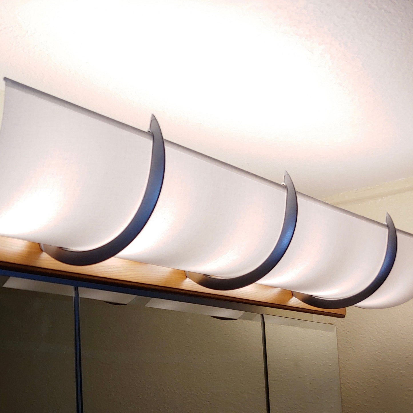 This is a white linen shade with 2 silver brackets over a beveled edge light. Usually on a beveled edge we can hide the bulbs but not the bottom of the fixture.
